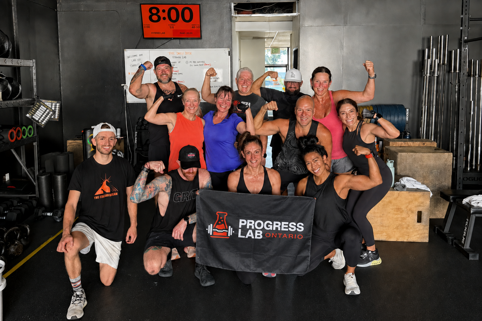 A group at Progress Lab poses together after training, holding a Progress Lab banner.